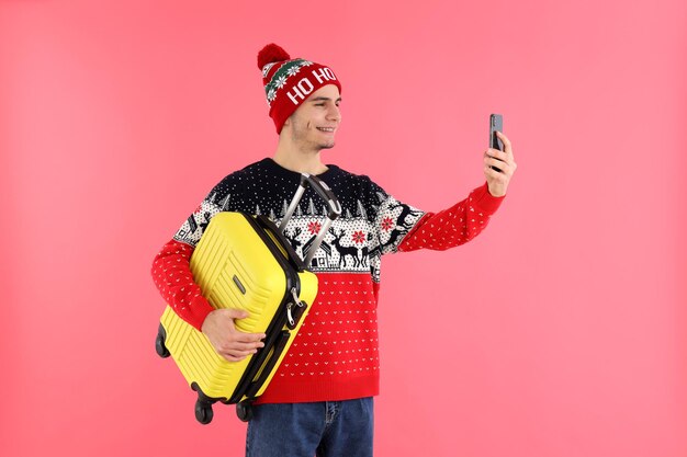 Kerl im Weihnachtspullover mit Gepäcktasche auf rosa Hintergrund
