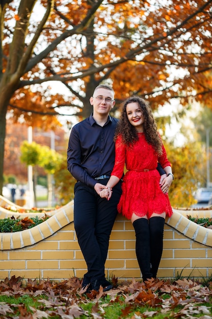 Kerl in einem schwarzen Hemd und ein Mädchen mit Locken in einem roten Kleid auf einer herbstlichen Stadtgasse