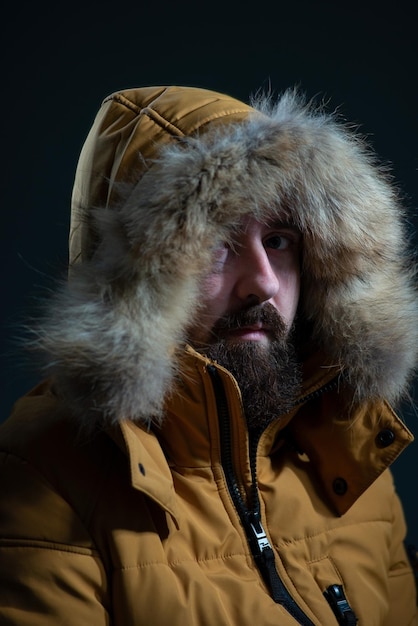 Kerl in einer Daunenjackenhaube mit pelzgelber Jacke auf grauem Hintergrund