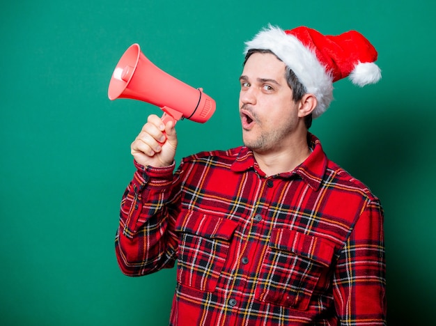 Kerl in Weihnachtsmütze und Gesichtsmaske mit Megaphon auf Grün