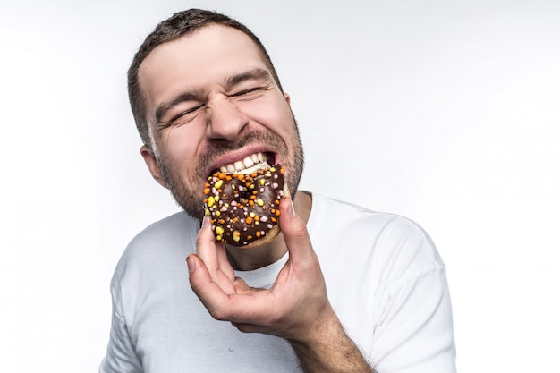 Kerl isst leckeren kleinen Donut mit Schokolade bedeckt