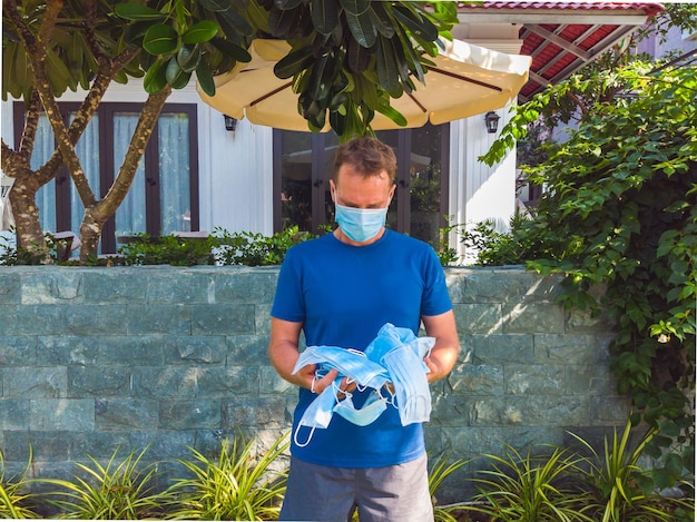 Kerl mit medizinischer Maske Draußen im Garten in der Nähe des modernen Sommerhauses spazieren will Atem wegwerfen Maske warten auf das Ende der Quarantäne Covid 19 Isolation und den Beginn des normalen Lebens wieder