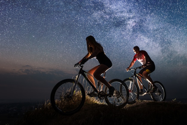 Kerl und Mädchen, die Fahrräder auf dem Hügel nachts fahren