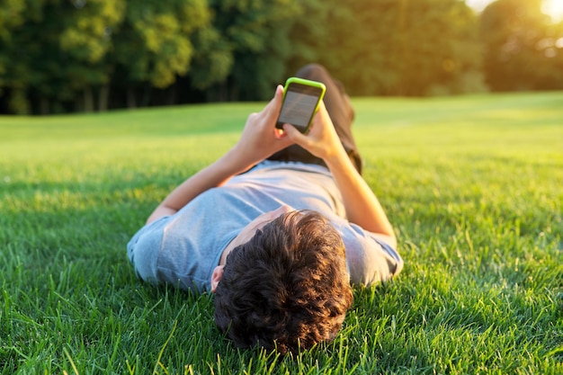 Kerljugendlicher, der auf Gras mit Smartphone liegt