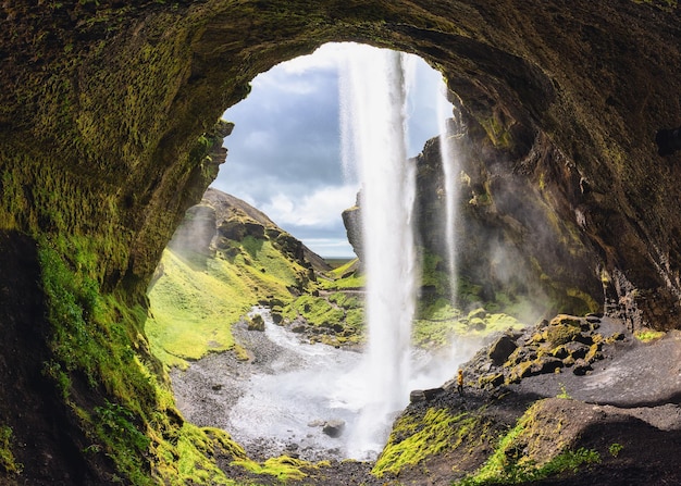 Kernufoss-Wasserfall, der von der Klippe fließt, und Wanderer stehen im Sommer in Island
