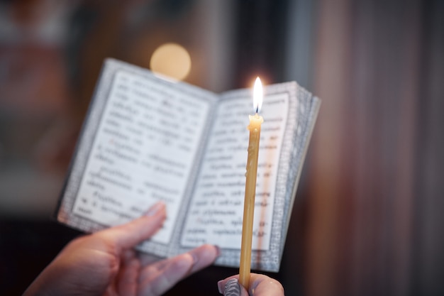 Kerze in der Hand und eine Gebetsbuchnahaufnahme in der orthodoxen Kirche