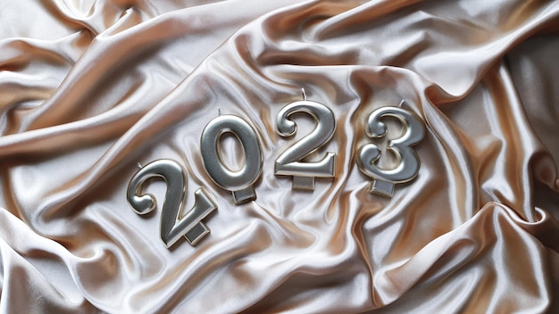 Kerzen in Form von Zahlen 2023 liegen auf einem goldenen Seidenstoff