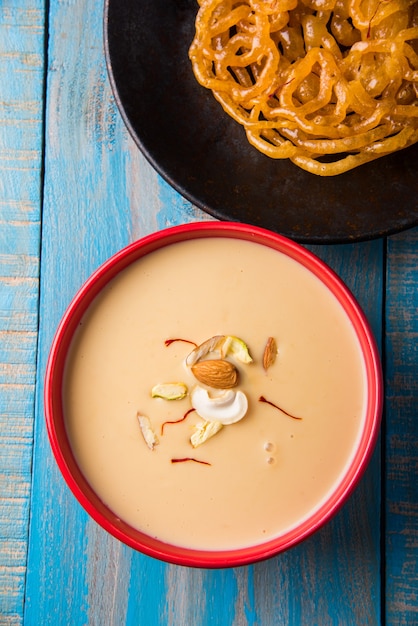 Kesari Jalebi o Jilbi con Rabdi es una deliciosa receta india que se sirve como postre en festivales o bodas, servida en plato y cuenco sobre fondo de colores o madera. Enfoque selectivo