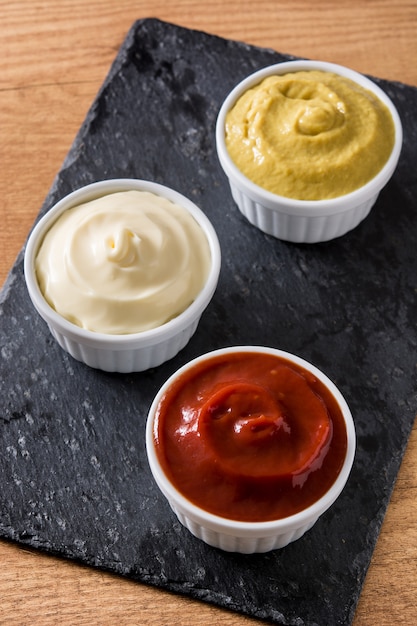 Ketchup, Senf und Mayonnaise in Schalen auf schwarzem Schiefer