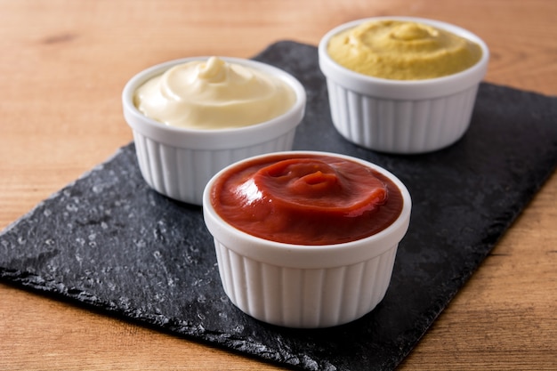 Ketchup, Senf und Mayonnaise in Schalen auf schwarzem Schiefer