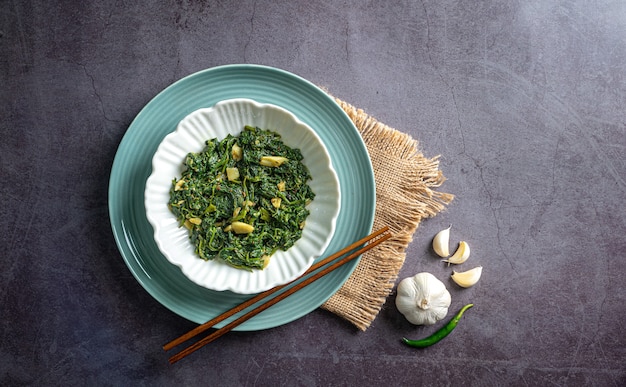 keto diet food espinafre curry em uma tigela branca e uma placa azul com chopstick de alho e pimenta na vista de cima da mesa de madeira azul