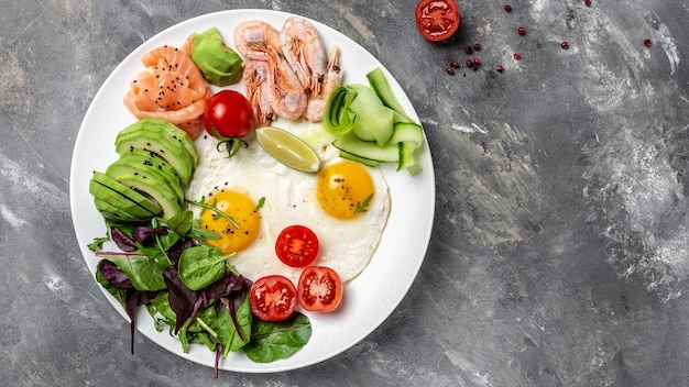 Ketobreakfast Lachs, gekochte Garnelen, Garnelen, Spiegeleier, frischer Salat, Tomaten, Gurken und Avocado. Konzept der gesunden Ernährung. Menürezeptplatz für Text, Draufsicht.