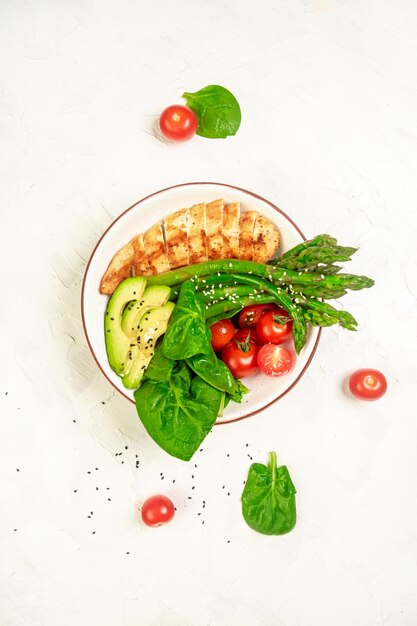 Ketogenes Diätfrühstück Gegrilltes Hähnchenfilet mit Salat, frischen Tomaten, Spargel und Avocado, vertikales Bild, Draufsicht, Platz für Text