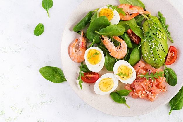 Ketogenes Diätfrühstück. Salzlachssalat mit gekochten Garnelen, Garnelen, Tomaten, Spinat, Eiern und Avocado.