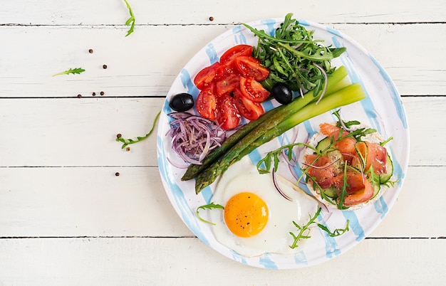 Ketogenes Frühstück Frühstück Spiegelei knusprige Brote mit lachsgrünem Spargel, frischen Tomaten und roten Zwiebeln auf weißem Teller Draufsicht flach gelegt