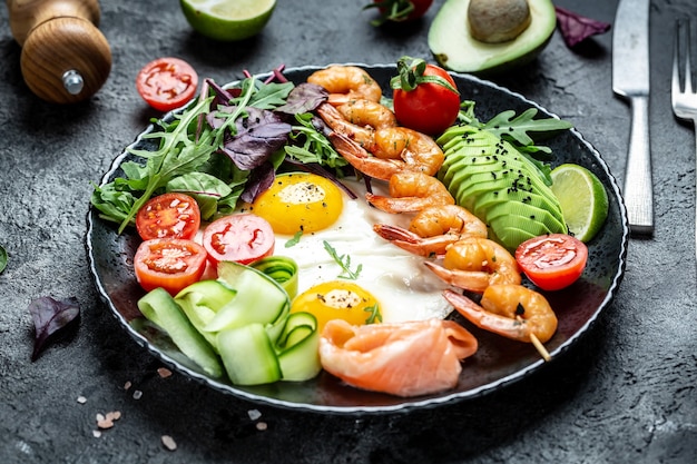 Ketogenes Frühstück. Keto-Low-Carb-Lachs, gegrillte Garnelen, Garnelen, Spiegeleier, frischer Salat, Tomaten, Gurken und Avocado. ketogene Ernährung. Ansicht von oben.