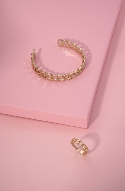 Kettenform goldenes Armband und Ring auf rosa Oberfläche