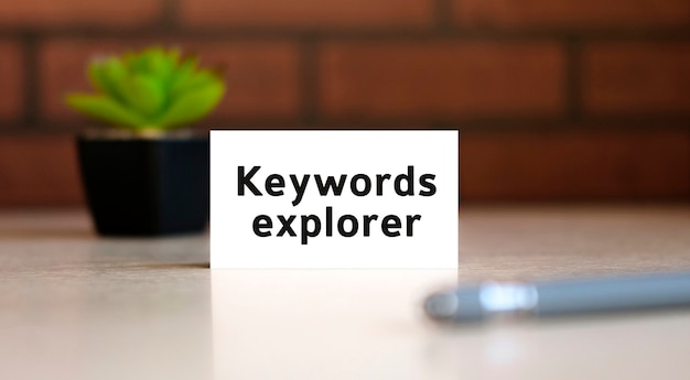 Keywords Explorer - Text des Geschäftskonzepts auf weißer Liste und mit Stift und einem schwarzen Topf mit einer Blume dahinter