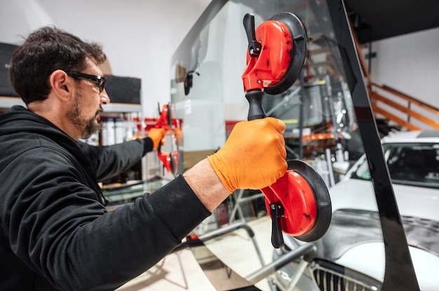Foto kfz-techniker arbeiter, der windschutzscheibe oder windschutzscheibe eines autos in der autowerkstattgarage ersetzt.