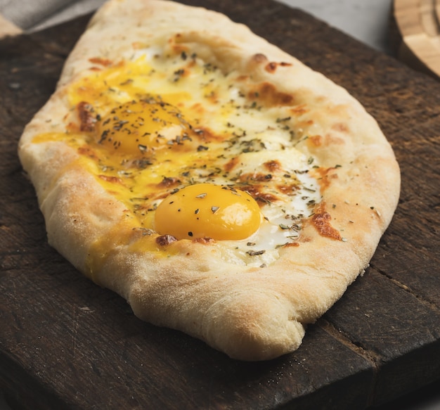 Khachapuri adjarian al horno con yema de huevo entera sobre tabla de madera, plato tradicional, cerrar