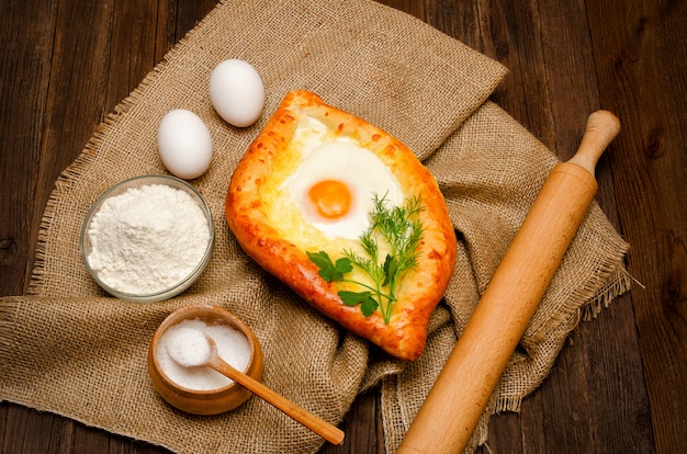 Foto khachapuri com ovos de saco, sal, farinha e ovos na mesa de madeira