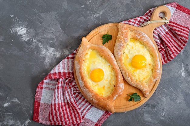 Khachapuri em Adjarian. Cozinha tradicional georgiana e armênia. Torta aberta com queijo suluguni e gema de ovo na forma de um barco em uma placa de madeira. A vista de cima