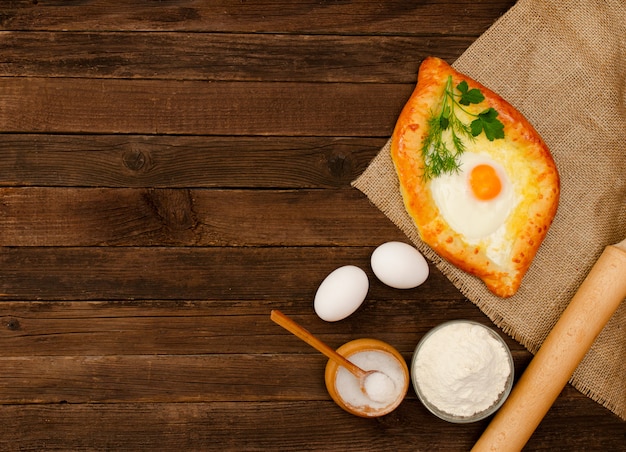 Khachapuri con huevos en tela de saco, sal, harina, huevos y perejil en la mesa de madera