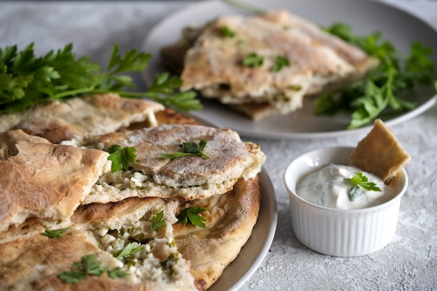 Khachapuri mit Hüttenkäse und Sauerrahm mit grüner Petersilie auf dem Teller