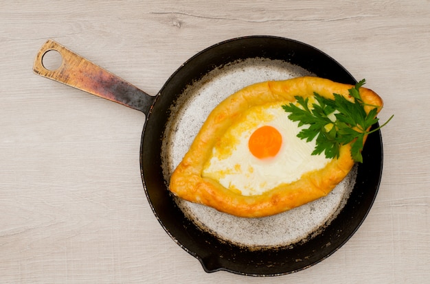 Khachapuri mit Käse und Ei in einer Bratpfanne auf einem hellen Holztisch