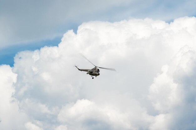 Khaki-Militärhubschrauber fliegt in den blauen Himmel mit Wolken