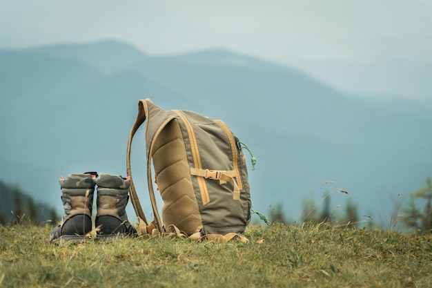 Khakifarbene Stiefel und Rucksack, die auf einem Gras auf einem Berghügel stehen. Wandertourismuskonzept