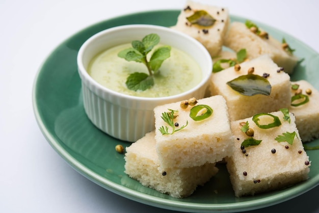 Khaman White Dhokla hecho de arroz o urad dal es una receta popular de desayuno o bocadillos de Gujarat, India, que se sirve con salsa picante verde y té caliente. Enfoque selectivo