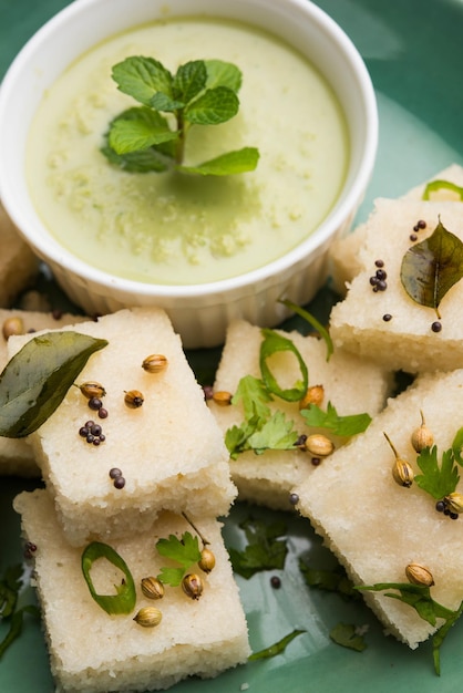 Khaman White Dhokla hecho de arroz o urad dal es una receta popular de desayuno o bocadillos de Gujarat, India, que se sirve con salsa picante verde y té caliente. Enfoque selectivo