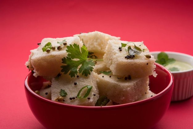 Khaman White Dhokla hecho de arroz o urad dal es una receta popular de desayuno o bocadillos de Gujarat, India, que se sirve con salsa picante verde y té caliente. Enfoque selectivo