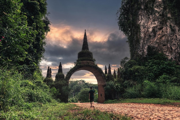 Khao Na Nai Luang Dharma Park, Suratthani, Thailand. Touristischer Mann, der morgens zum alten Bogentor mit buntem Himmel geht