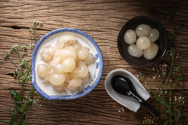 Khao Niew Piak Lam Yai, sobremesa tailandesa, arroz doce com longan e creme de coco em fundo de textura de madeira natural rústica, vista superior