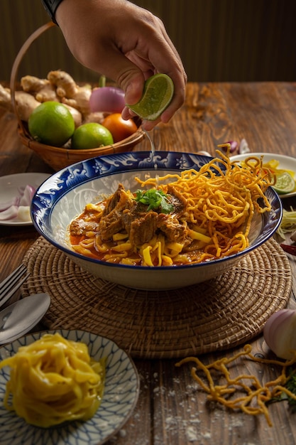 Foto khao soi comida tailandesa do norte em uma mesa de madeira e utensílios de cozinha