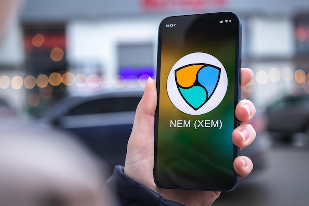 Kharkov Ukraine 2. Februar 2022 Nem XEM Münzsymbol Handel mit Kryptowährung digitales und virtuelles Geld Mobile Banking Hand mit Smartphone-Bildschirm mit Krypto-Symbol Nahaufnahme