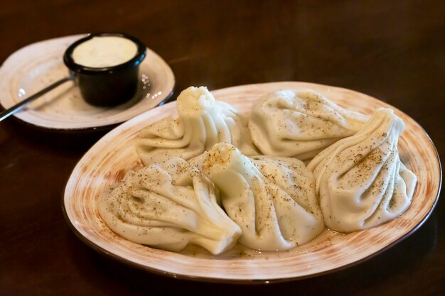 Khinkali - bolinhos georgianos tradicionais em um prato branco com molho de creme de leite branco em uma mesa de madeira no restaurante foco suave, close-up