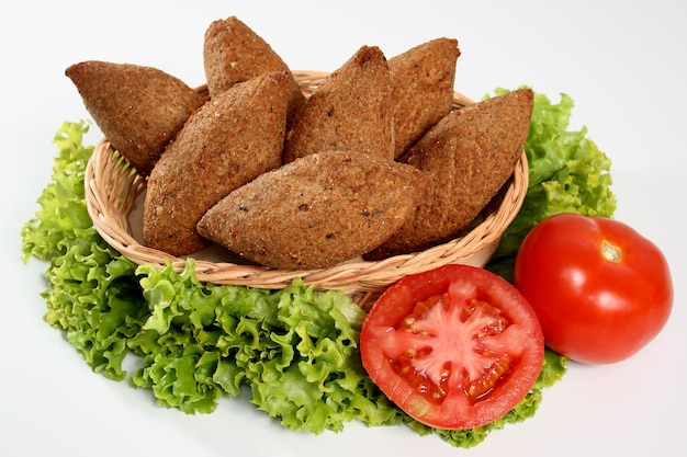 Kibbeh bocadillo tradicional árabe y brasileño (quibe) con rodajas de tomate sobre fondo blanco.