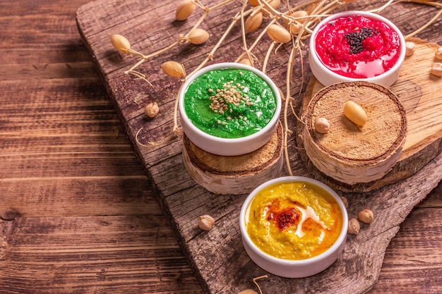 Kichererbsen-Hummus-Hintergrund. Verschiedene Geschmacksrichtungen mit verschiedenen Gemüsen und Gewürzen. Vintage-Holztisch, modernes hartes Licht, dunkler Schatten, Kopierraum