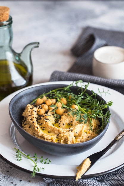 Kichererbsen-Hummus in der schwarzen Schüssel, verziert mit Sesam und Kichererbsengrün