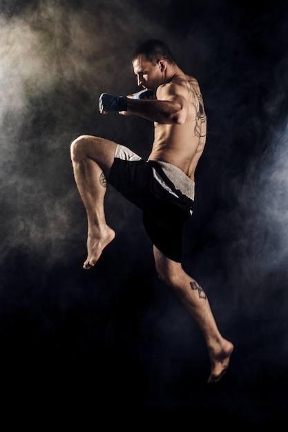 Kickbox muscular ou lutador tailandês muay socando no salto. fumaça