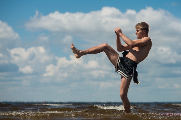 Kickboxer chuta ao ar livre no verão contra o mar.