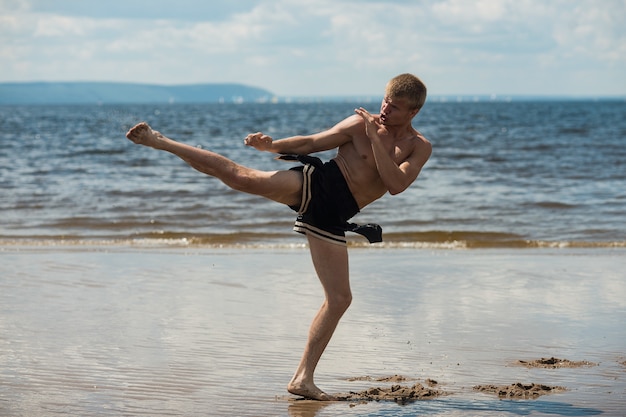 Kickboxer chuta ao ar livre no verão contra o mar.