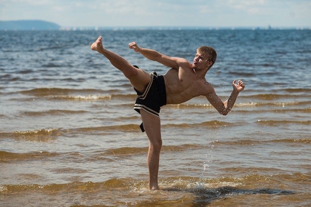 Kickboxer patea al aire libre en verano contra el mar.