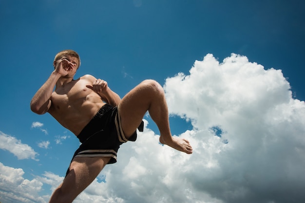 Kickboxer patea al aire libre en verano contra el mar.