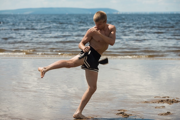 Kickboxer patea al aire libre en verano contra el mar,