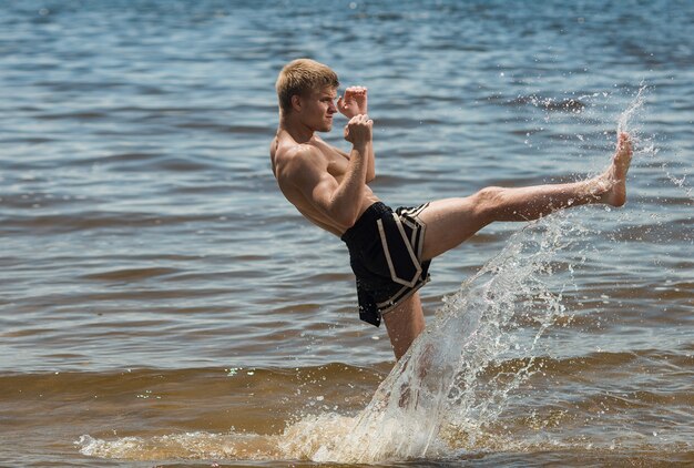 Kickboxer patea al aire libre en verano contra el mar,