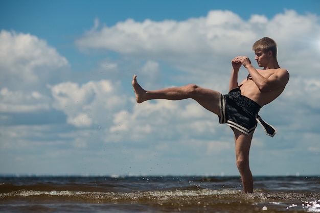 Kickboxer tritt im Sommer im Freien gegen das Meer.